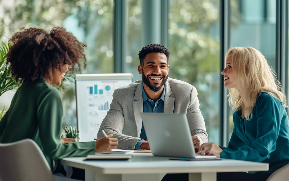 Business professionals discussing rebate management strategies in a modern office, analyzing financial data on a laptop and charts. Optimized rebate management software streamlines calculations, reconciliation, and reporting for increased accuracy and efficiency.