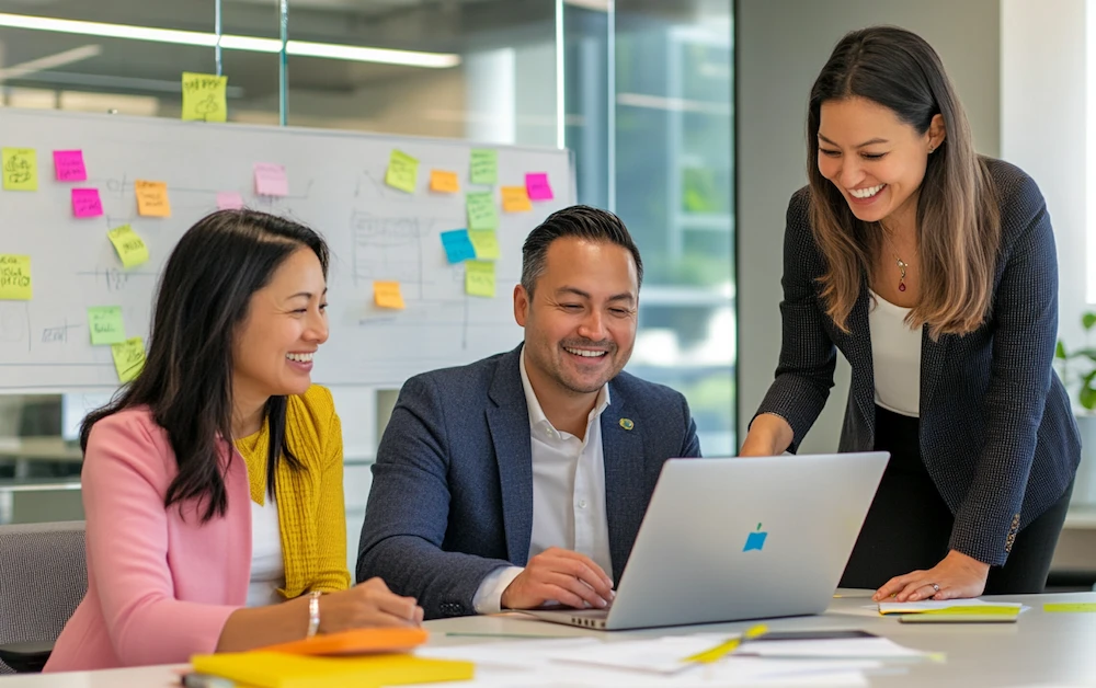 Finance professionals collaborating in a modern office, reviewing data on a laptop and discussing digital finance skills development, with a whiteboard of sticky notes in the background.