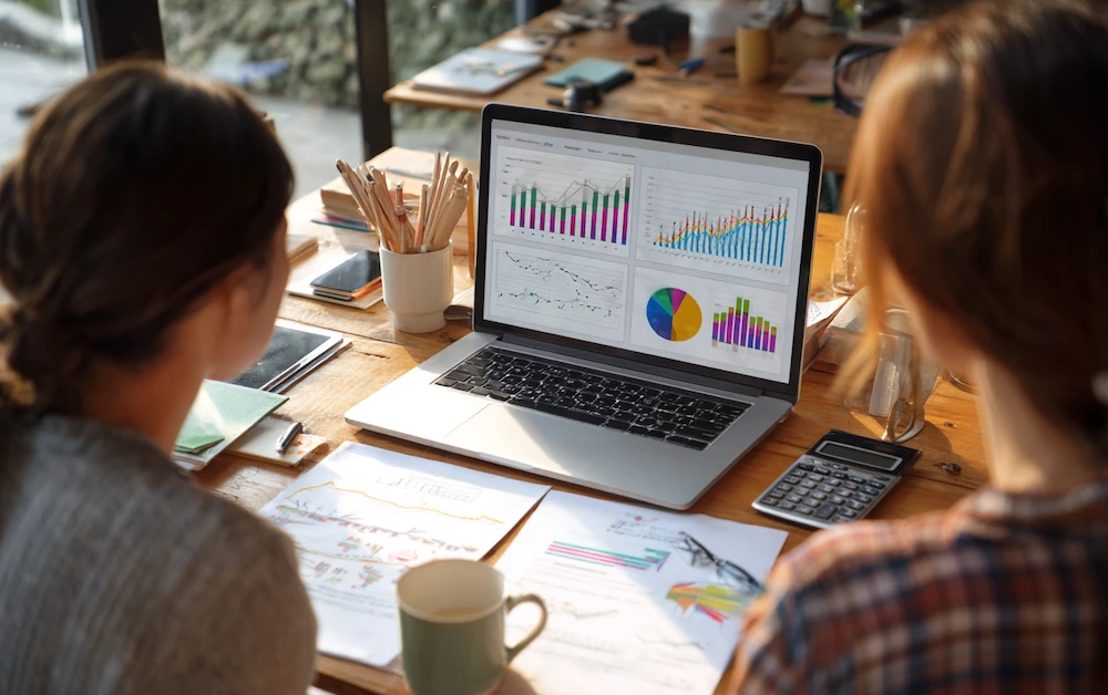 Two analysts reviewing charts and dashboards on a laptop during an automated data preparation workflow, streamlining data analysis and reporting in a collaborative workspace.
