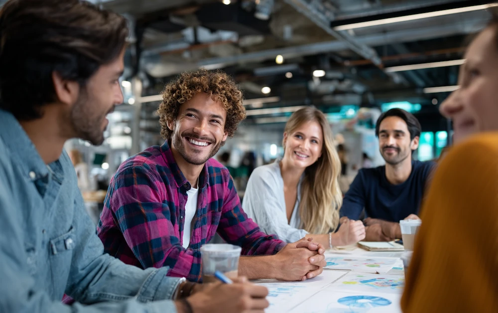 A diverse group of professionals collaborating around a table with charts and diagrams, embodying teamwork and innovation within a process excellence framework in a modern office setting.