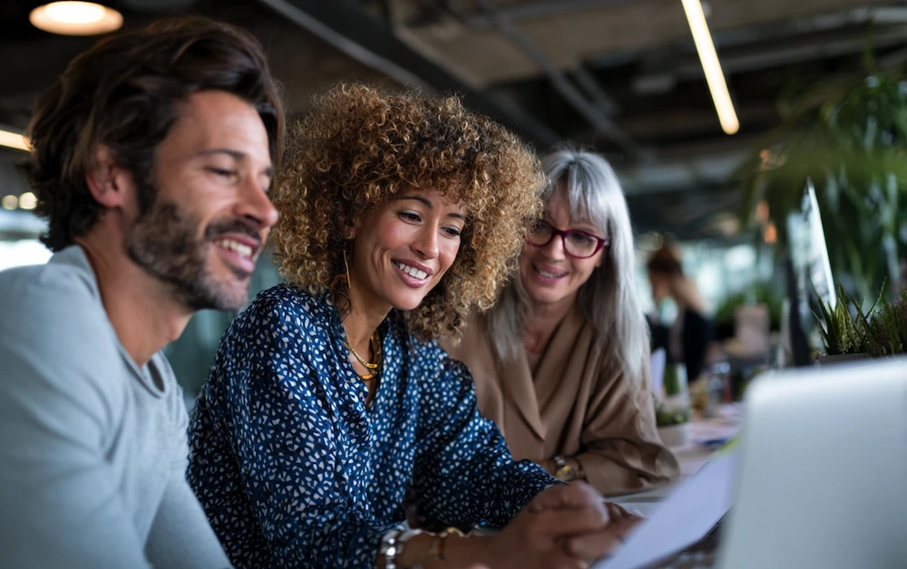Finance team collaborating on reconciliation accounting process, reviewing financial data and reports on a laptop in a modern office.