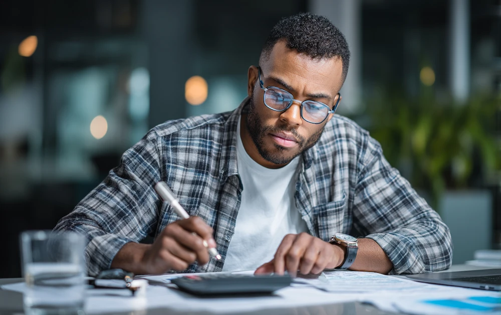 Finance professional reviewing a bank reconciliation statement using a calculator and paperwork at a desk — illustrating the process of verifying and matching financial records for accuracy.