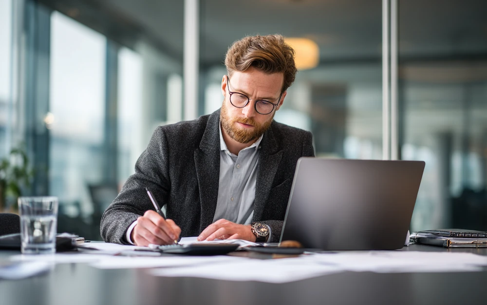 Finance professional calculating rebates at a desk with a laptop and paperwork in a modern office — illustrating how to calculate rebates accurately for business reporting.