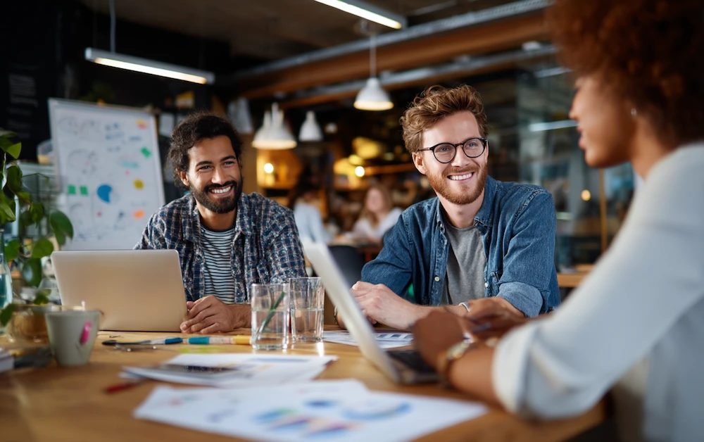 Team of diverse professionals collaborating on laptops in a modern office, surrounded by charts and documents, discussing strategies for implementing an operational excellence framework to improve business processes, drive efficiency, and achieve continuous improvement goals.