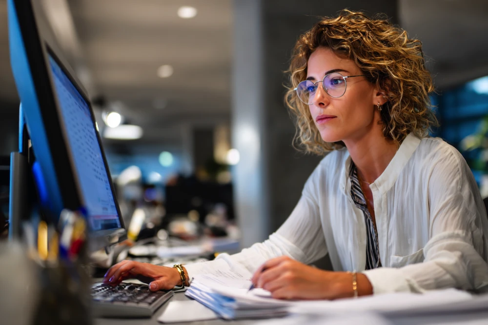 Finance professional using invoice reconciliation software on a desktop computer in a modern office, reviewing financial documents and ensuring accurate transaction matching.