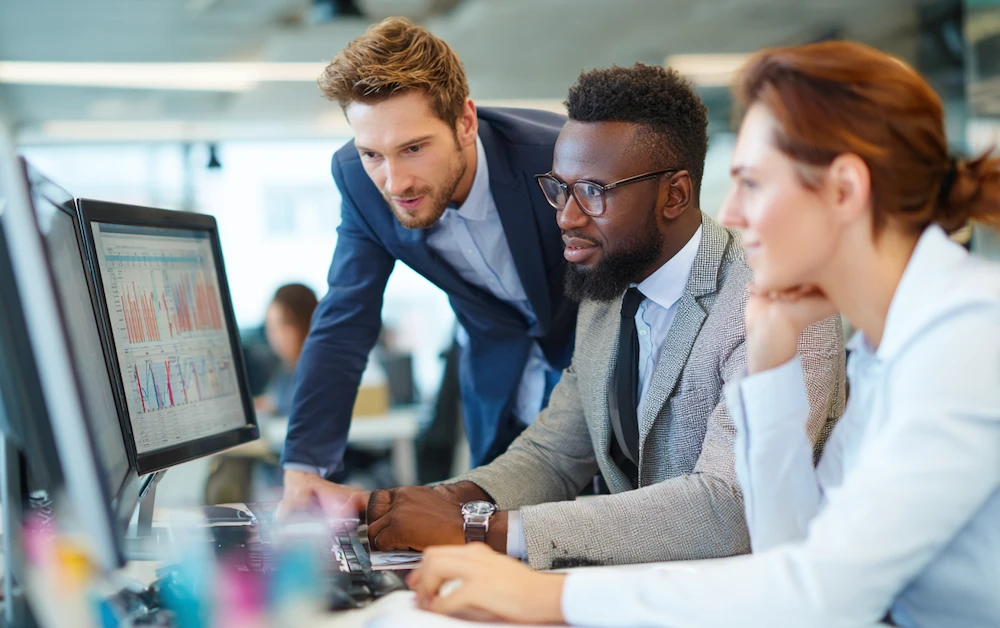 Team of financial analysts collaborating in a modern office, reviewing charts and graphs on computer monitors for financial data analysis and reporting.