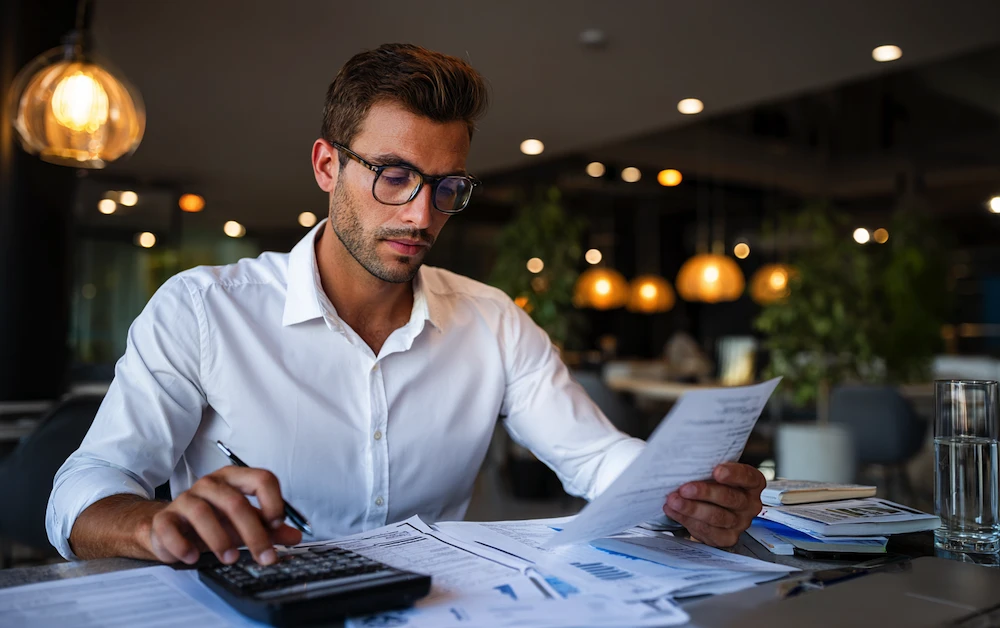 Accountant reviewing financial statements and using a calculator to perform cash reconciliation and ensure accurate cash flow reporting.