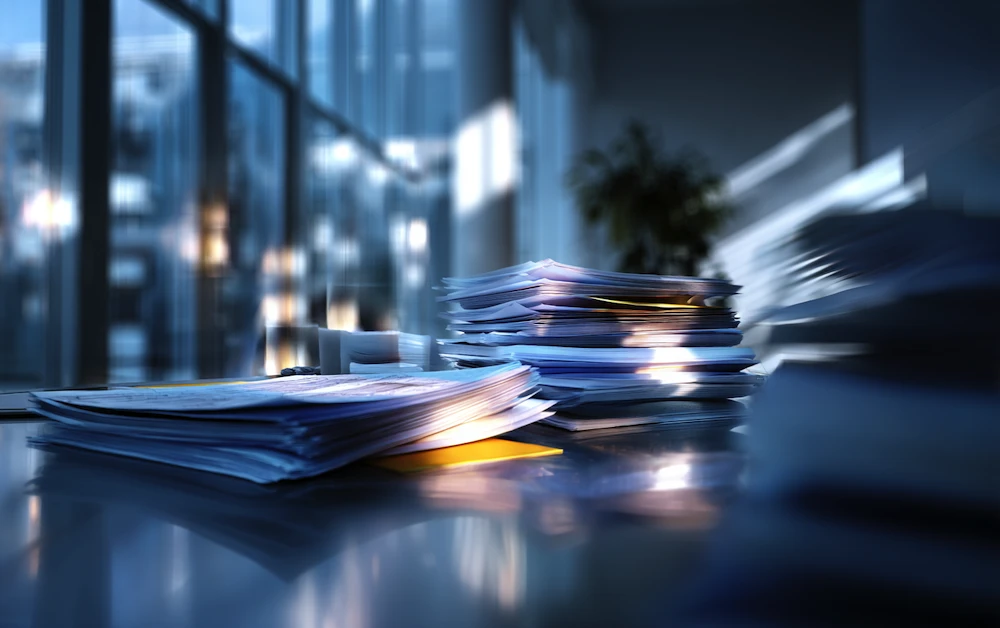 Stacks of financial documents piled on an office desk, illustrating the manual workload teams face when trying to reconcile accounts without automation.
