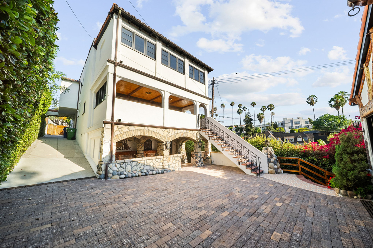 The driveway slopes down to a paver-tiled motor court.