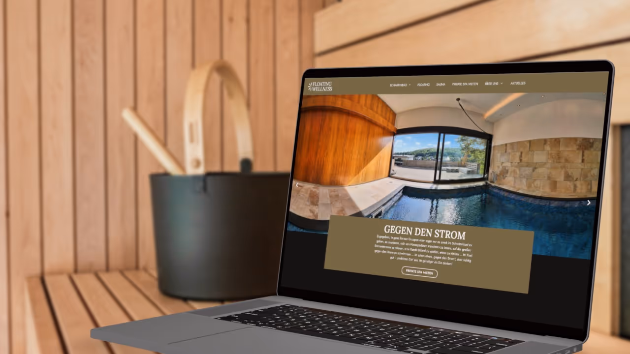Ein Laptop steht in einer Sauna, Hintergrund ist unscharf. Er zeigt die Startseite von Floating Wellness.