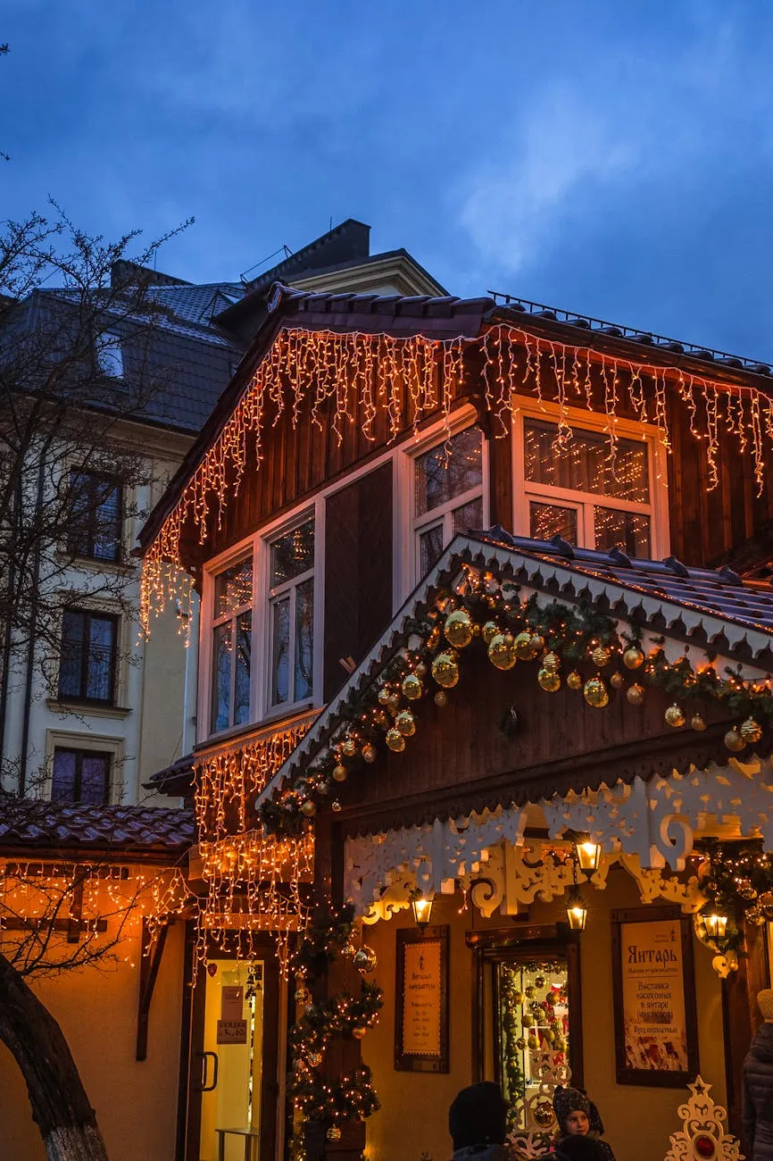 Christmas lights hanging along the eaves of a wooden house, with golden ornaments and garlands adorning the roof. The warm glow of the lights contrasts against the evening sky, creating a festive and inviting atmosphere.