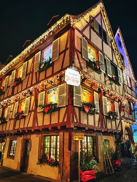 Traditional half-timbered building decorated with Christmas lights and red heart ornaments at night.