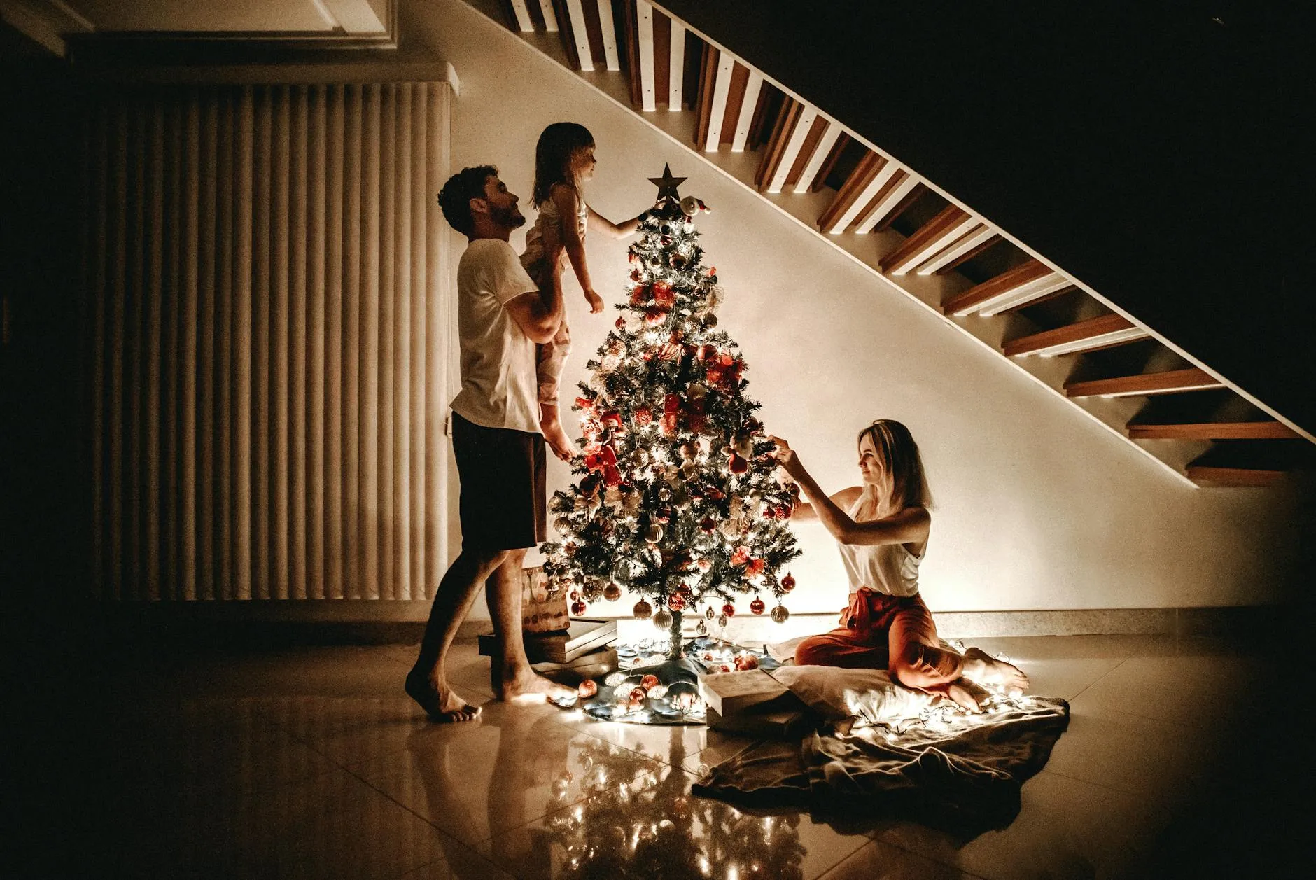 Family decorating the Christmas tree together, with warm holiday lights and decorations.