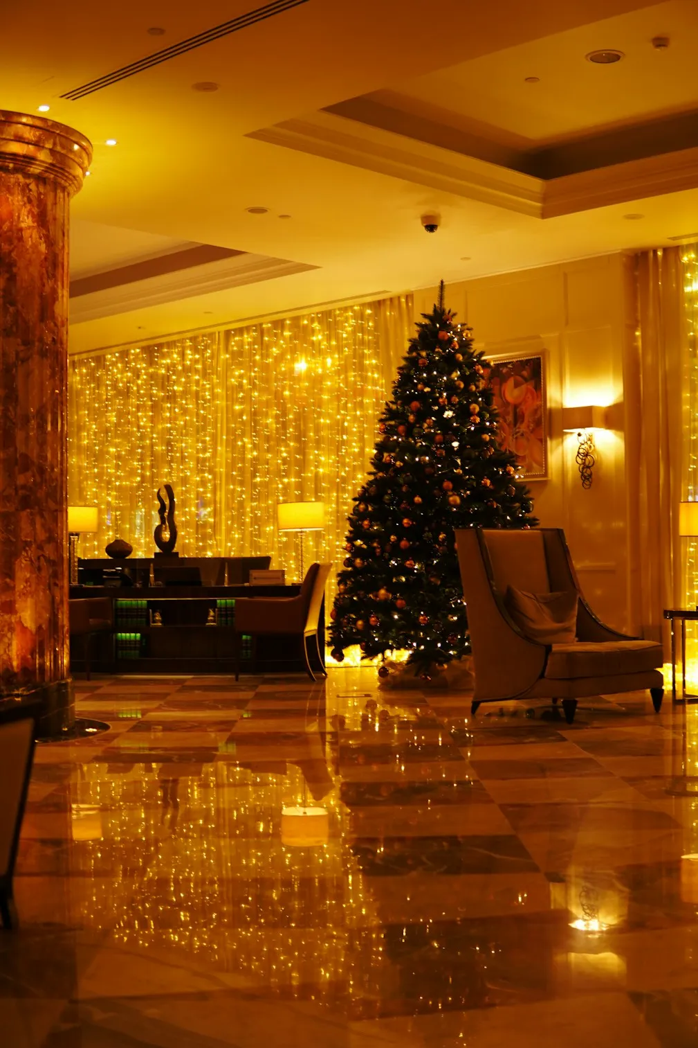 Elegant Christmas tree with warm golden lights and festive decorations in a luxurious indoor setting.