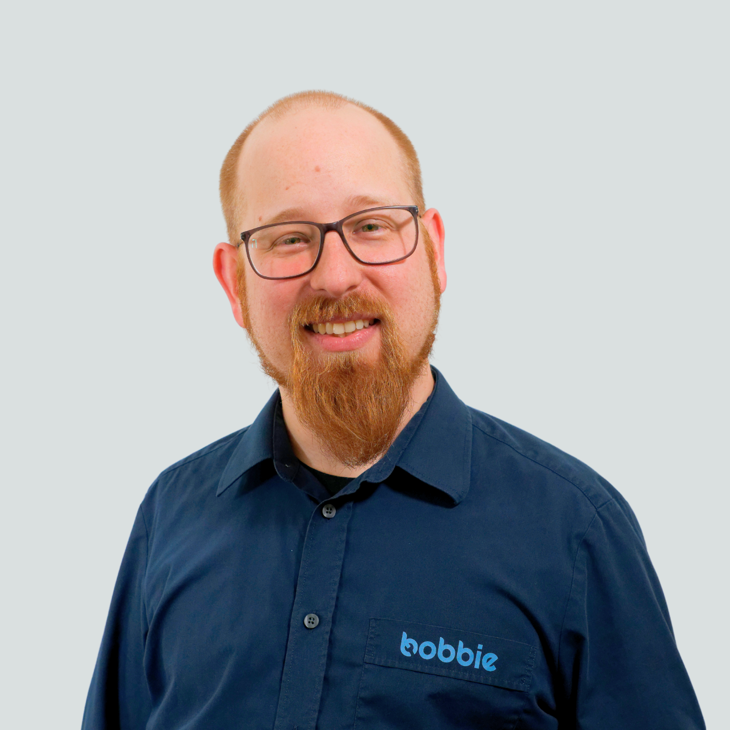 Smiling man with glasses, red beard, and Bobbie shirt against a plain light gray background.