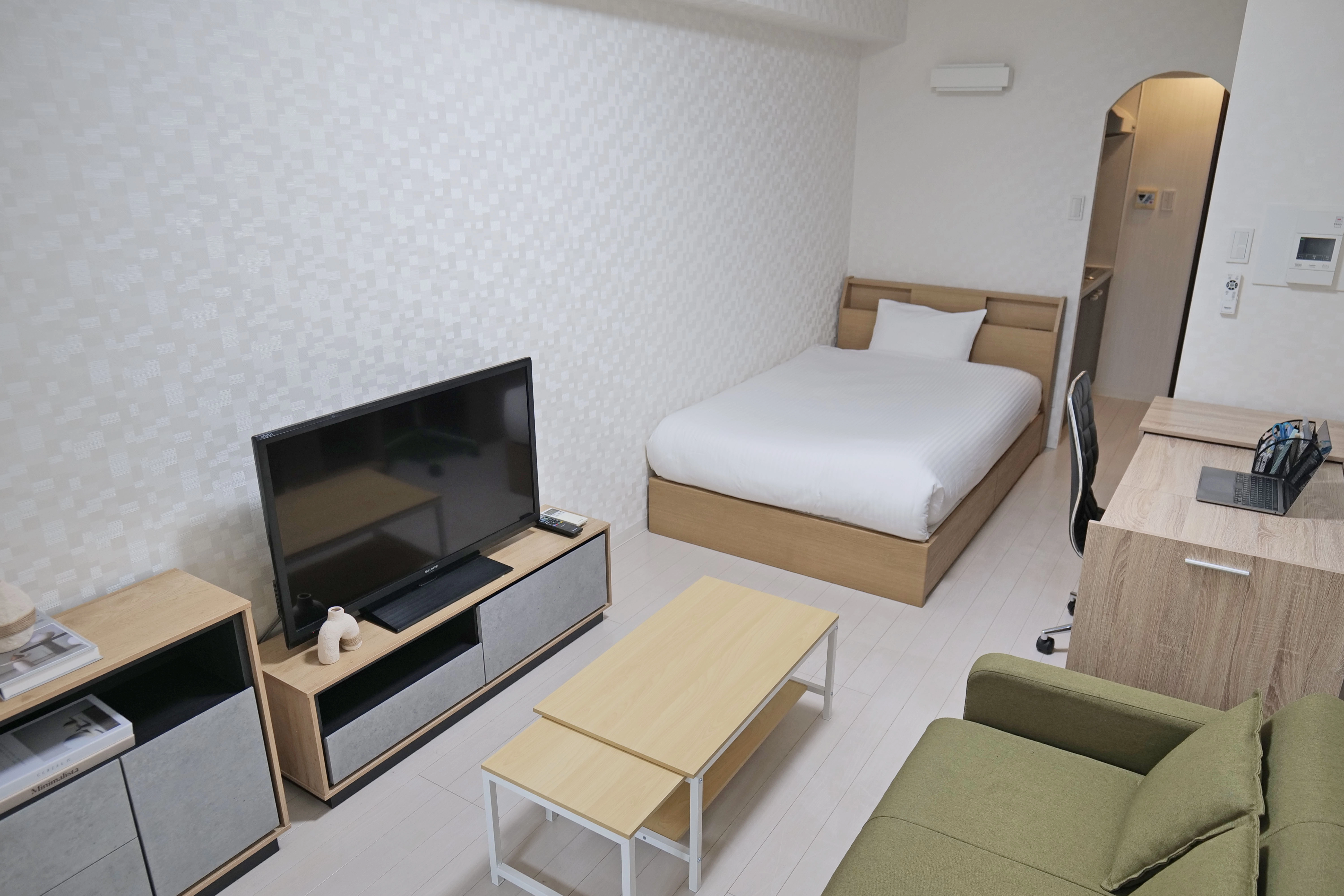 Cozy compact room featuring a semi-double bed, wooden floors, big shelf with tv, study desk and center table.