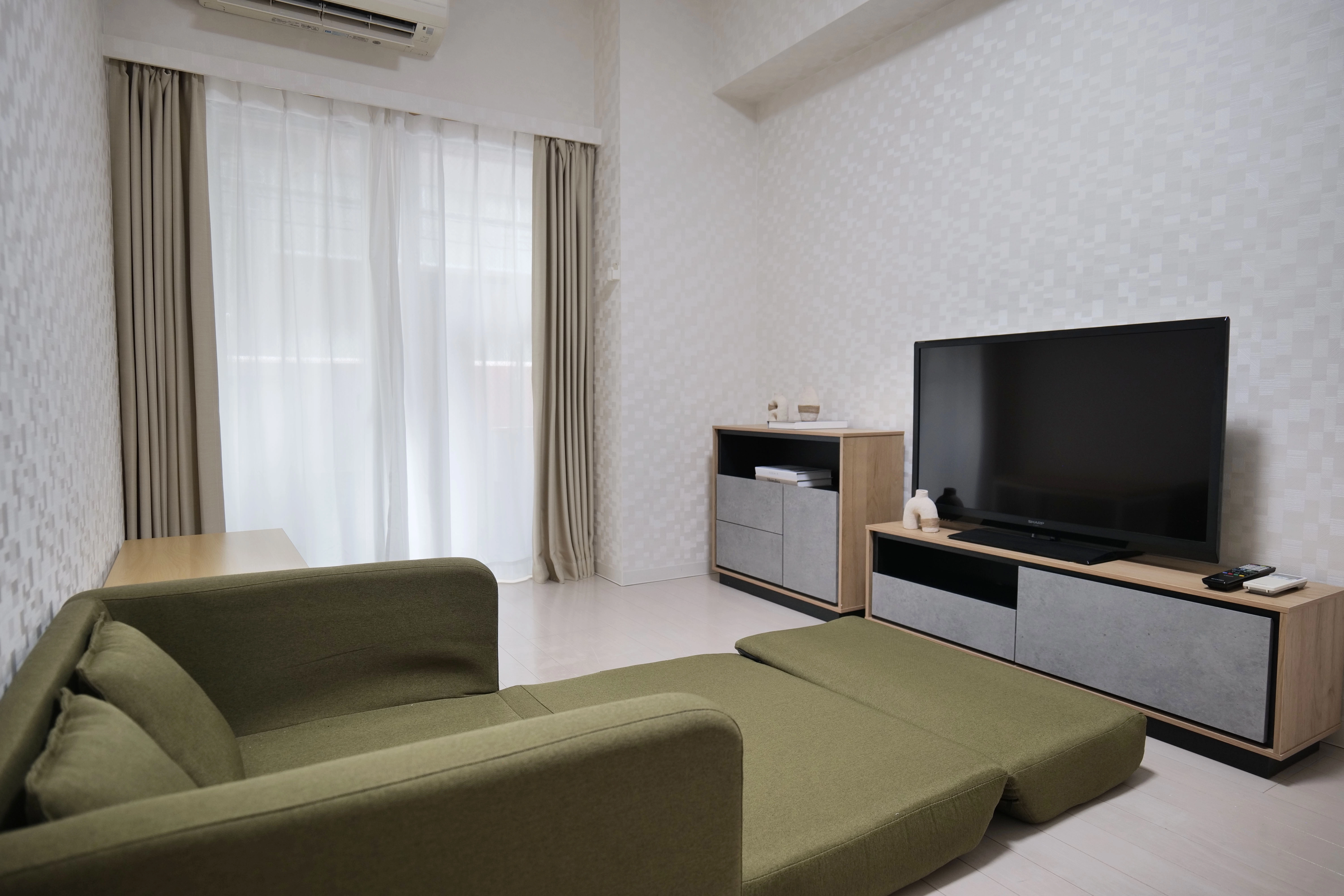 Modern compact bedroom with sofa bed, wooden floors, small TV stand, and center table.
