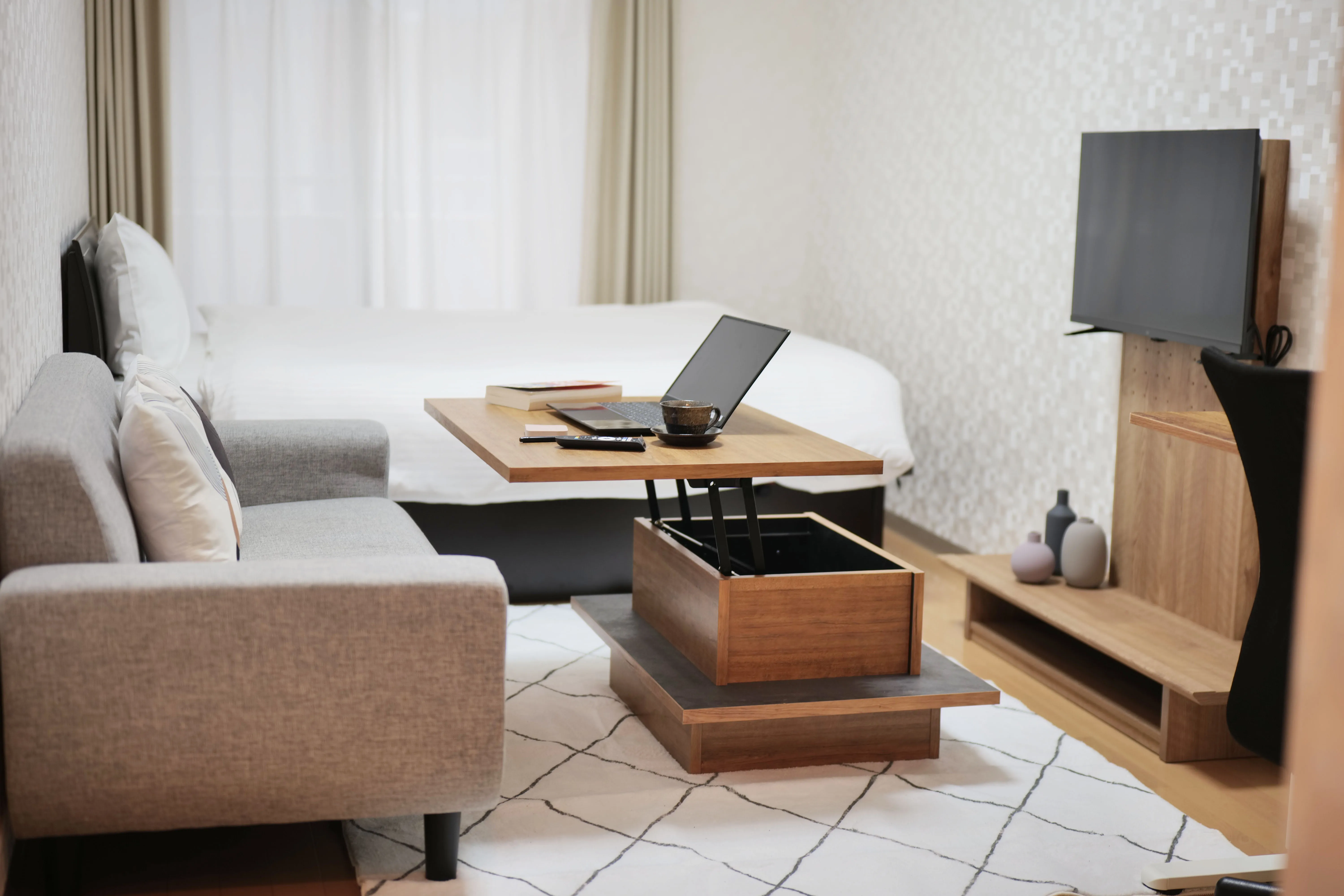 Small bedroom with semi-double bed, compact center table, TV stand, and wooden flooring.