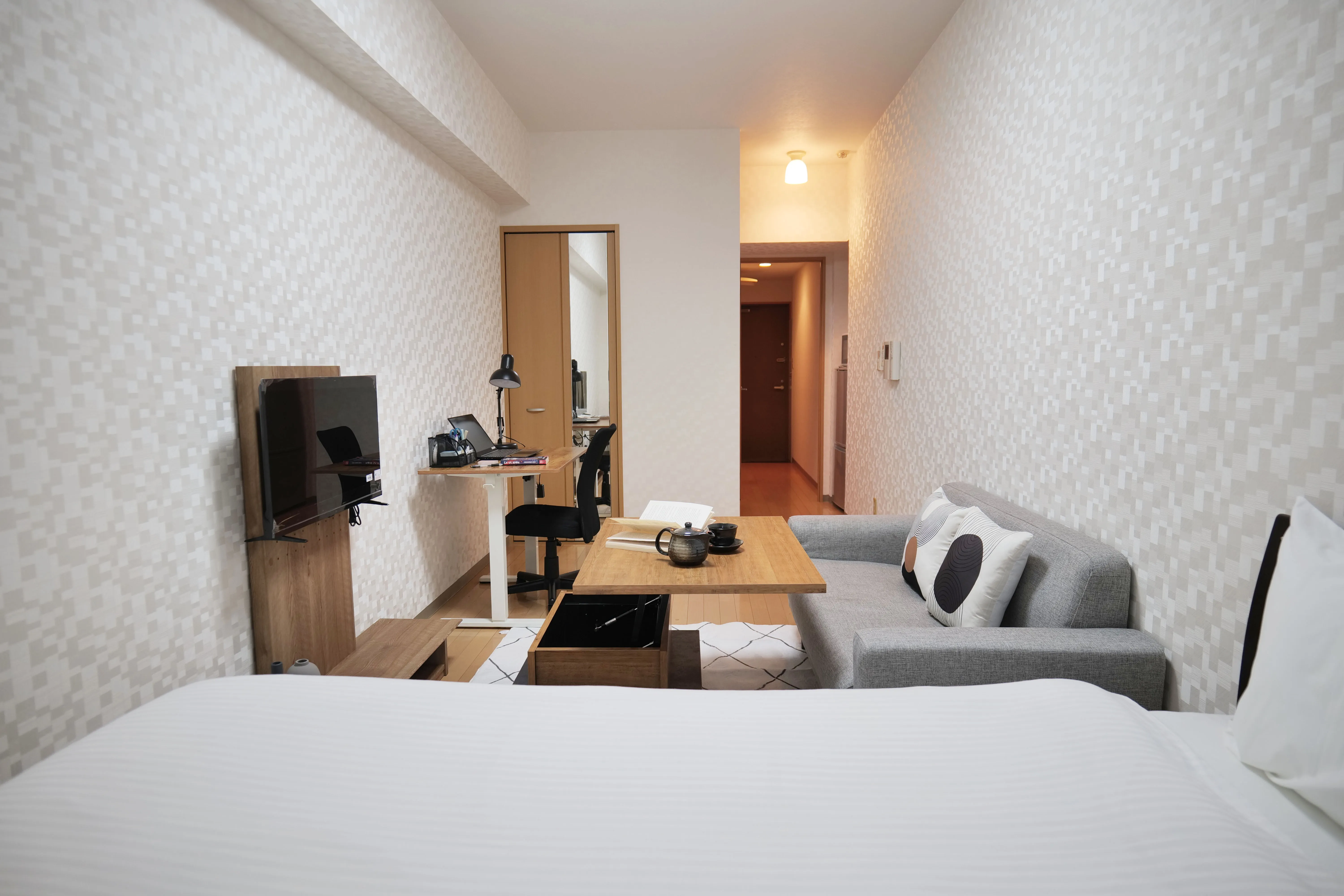 Cozy compact room featuring a semi-double bed, wooden floors, big shelf with tv, study desk and center table