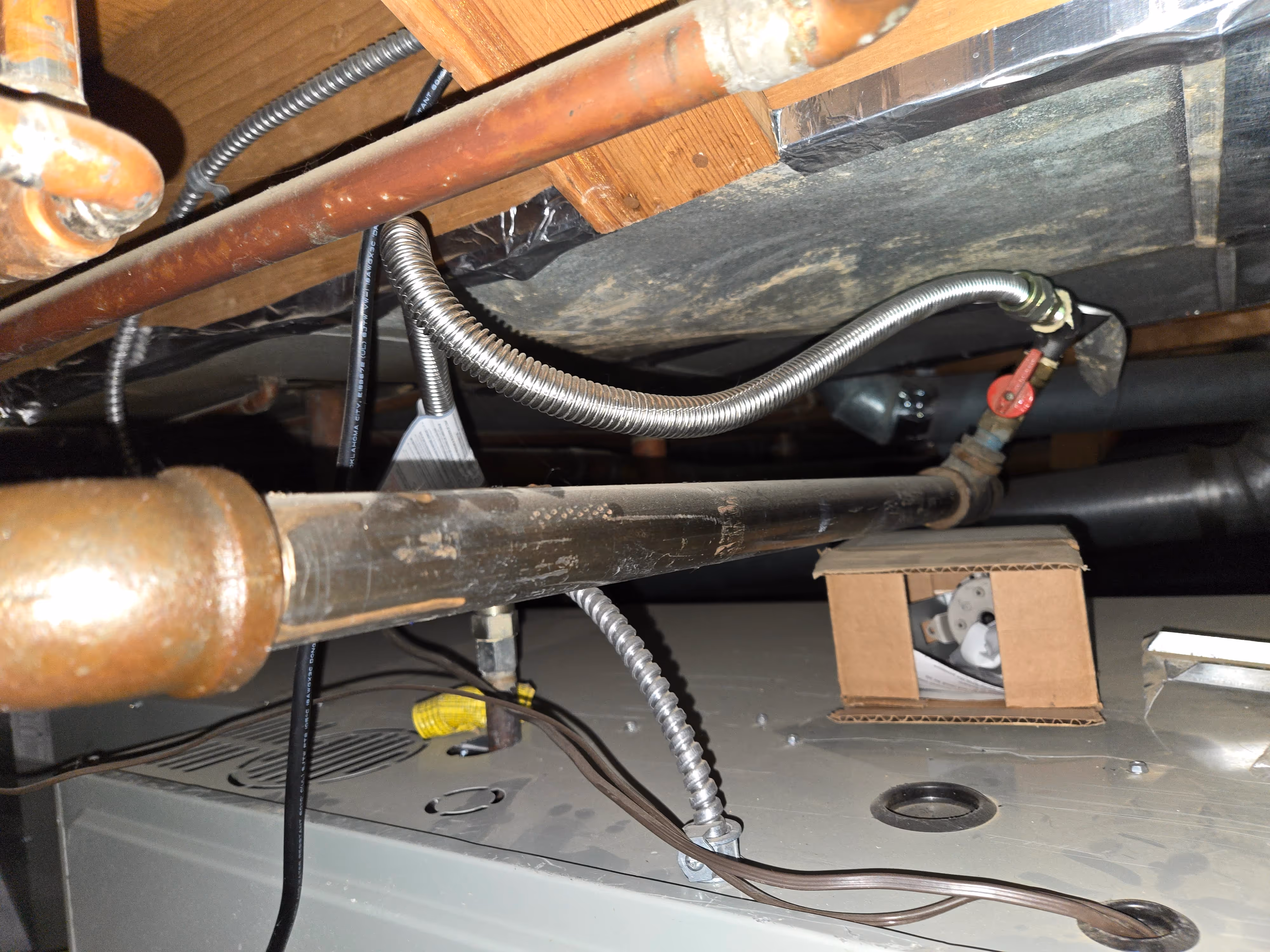 View of a basement ceiling showing exposed pipes, wires, and insulation.