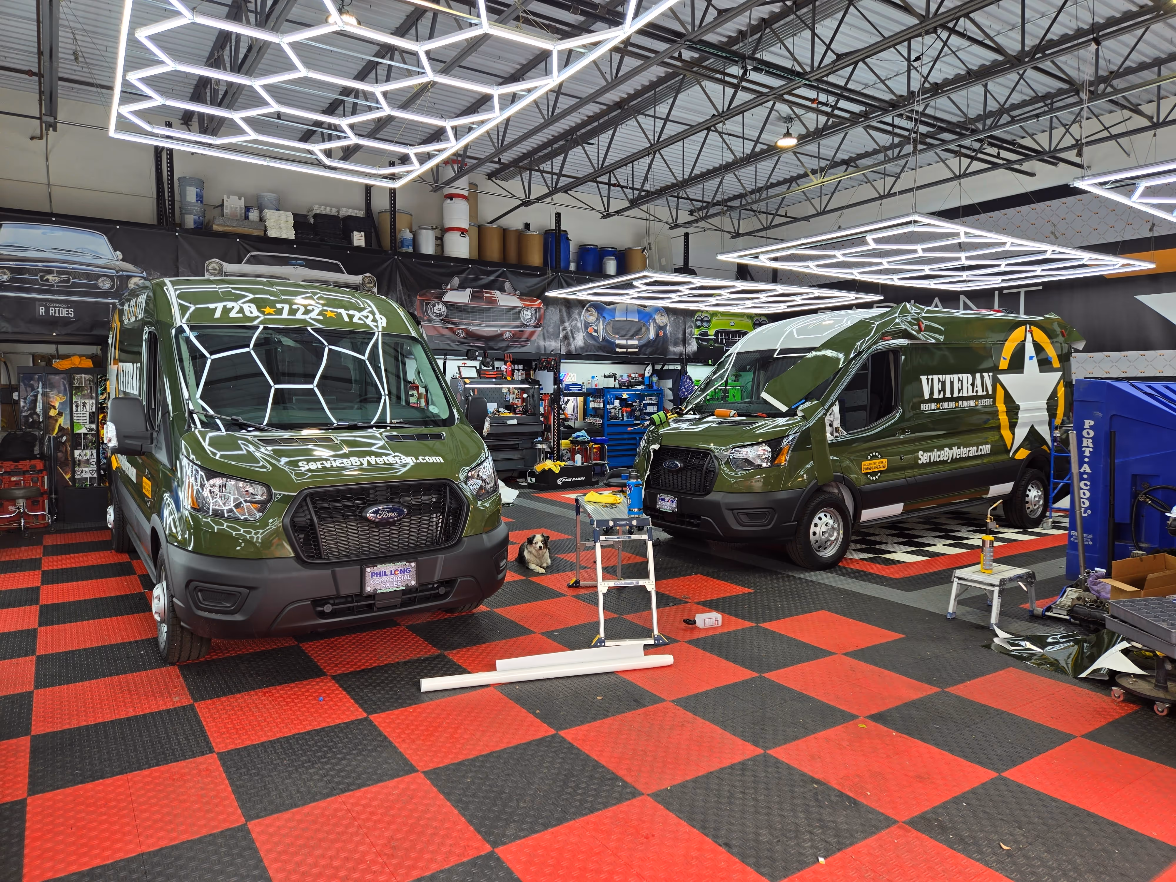 Two green service vans are parked in a garage with checkered floors and bright hexagonal lights.