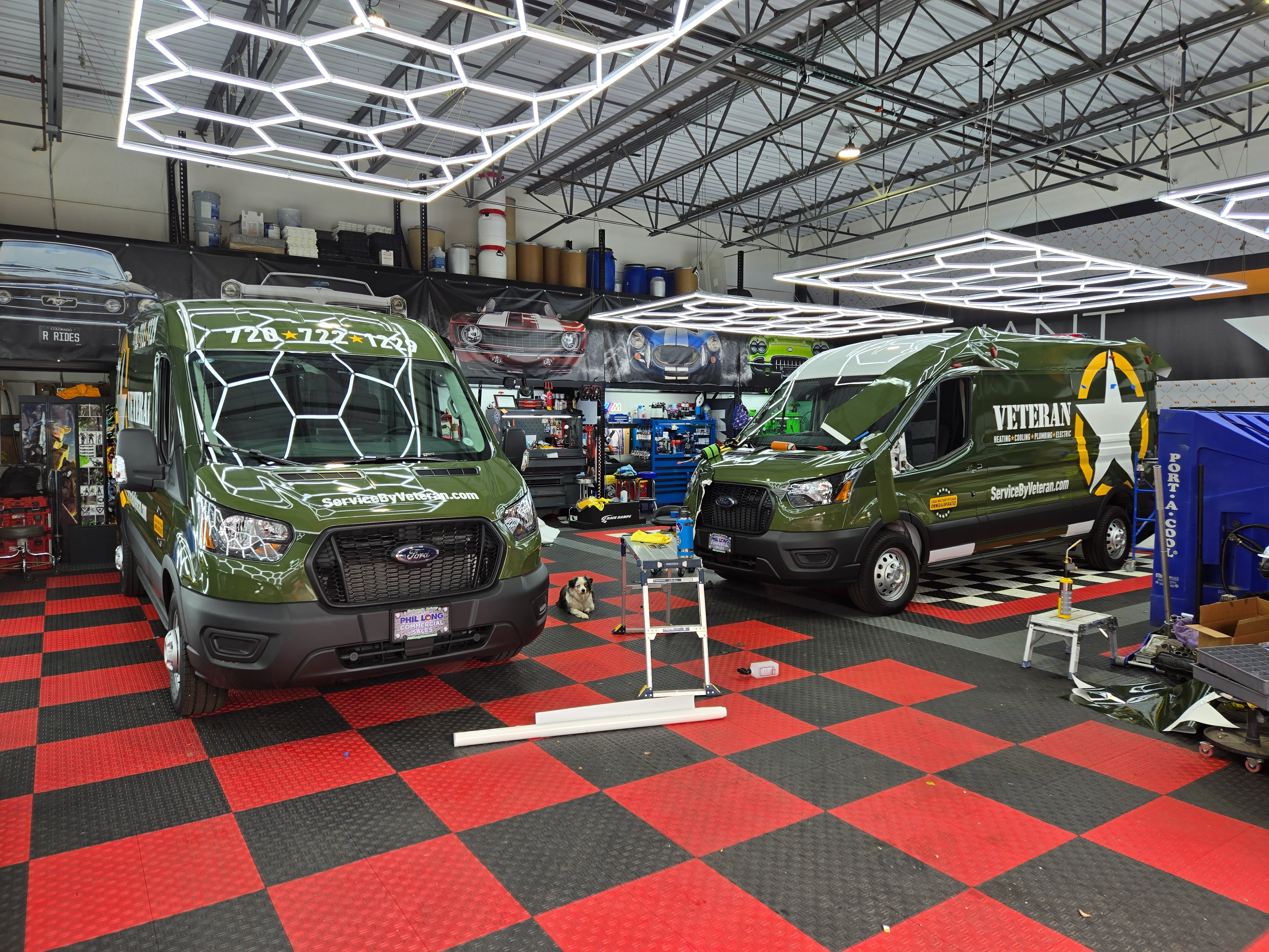 Two green service vans are parked in a garage with checkered floors and bright hexagonal lights.