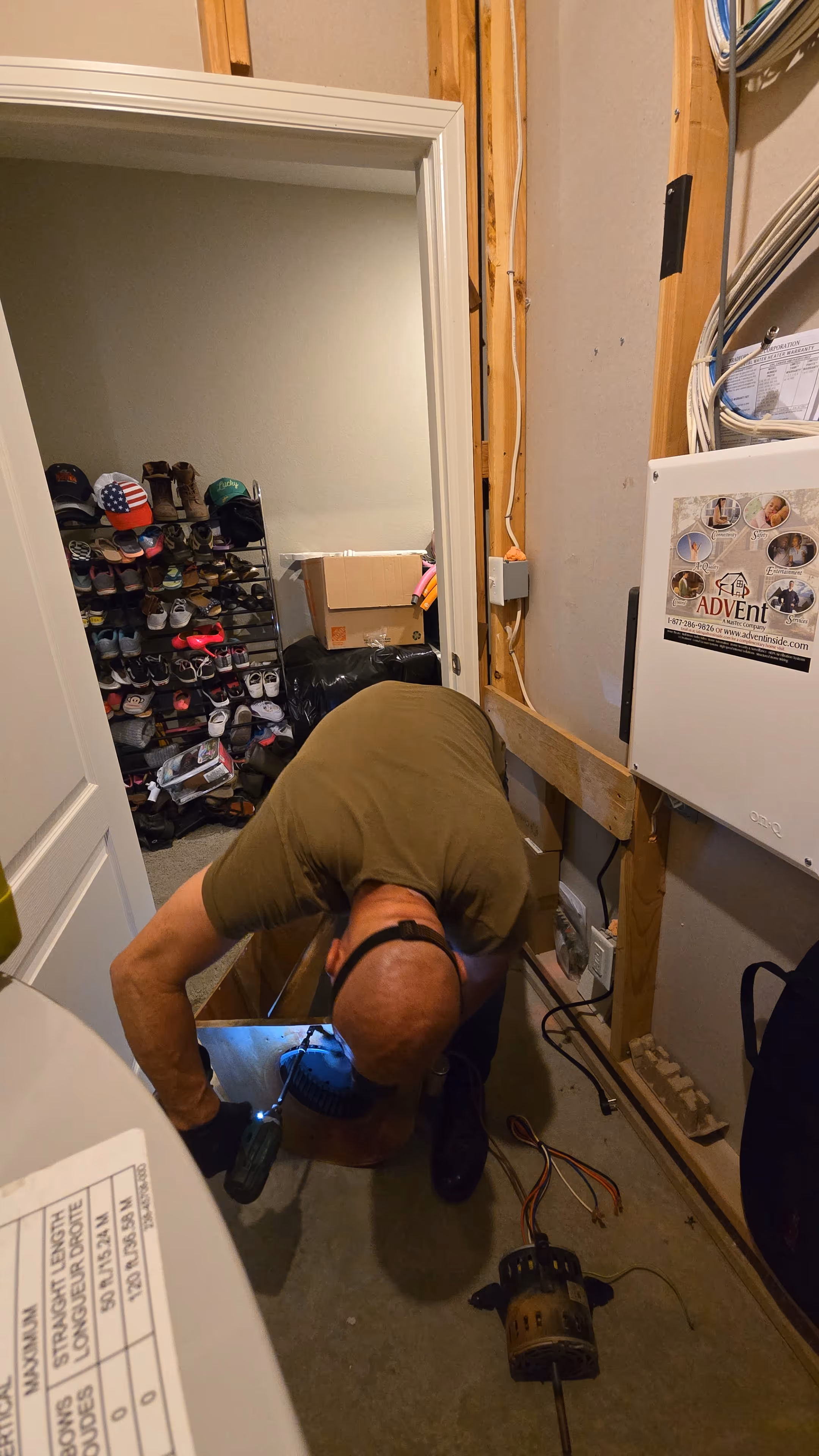 A person wearing a headlamp inspects equipment on the floor of a utility closet
