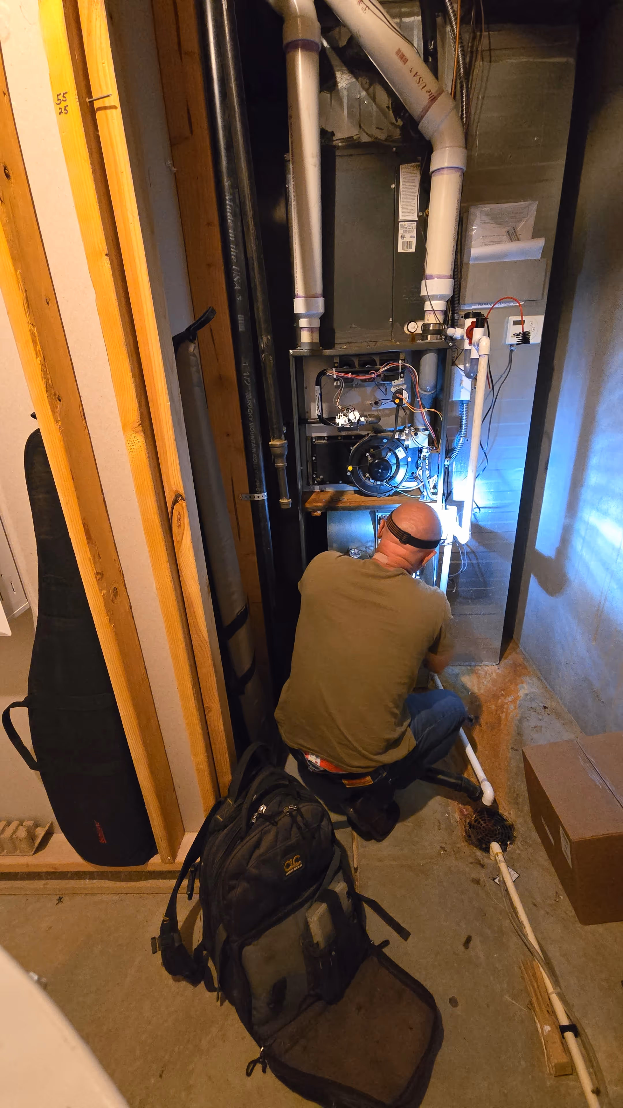 A person is crouched down, working on a furnace in a dimly lit space.