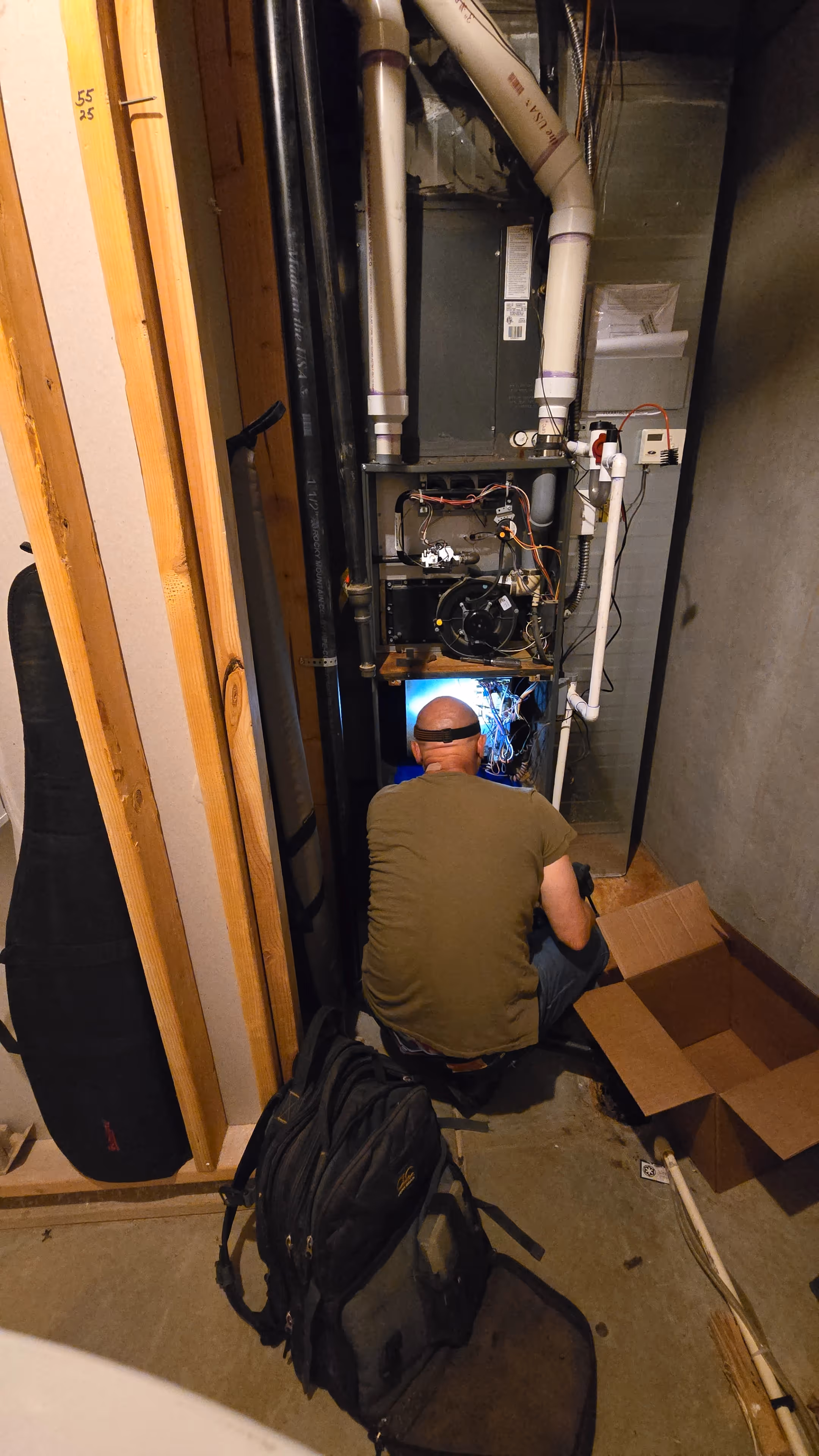 A man works diligently on a furnace inside a cramped room, surrounded by tools and equipment.