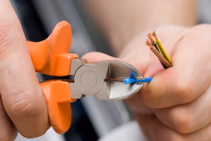 A close-up shot of a person's hands using wire strippers to cut and strip the insulation from a group of electrical wires.
