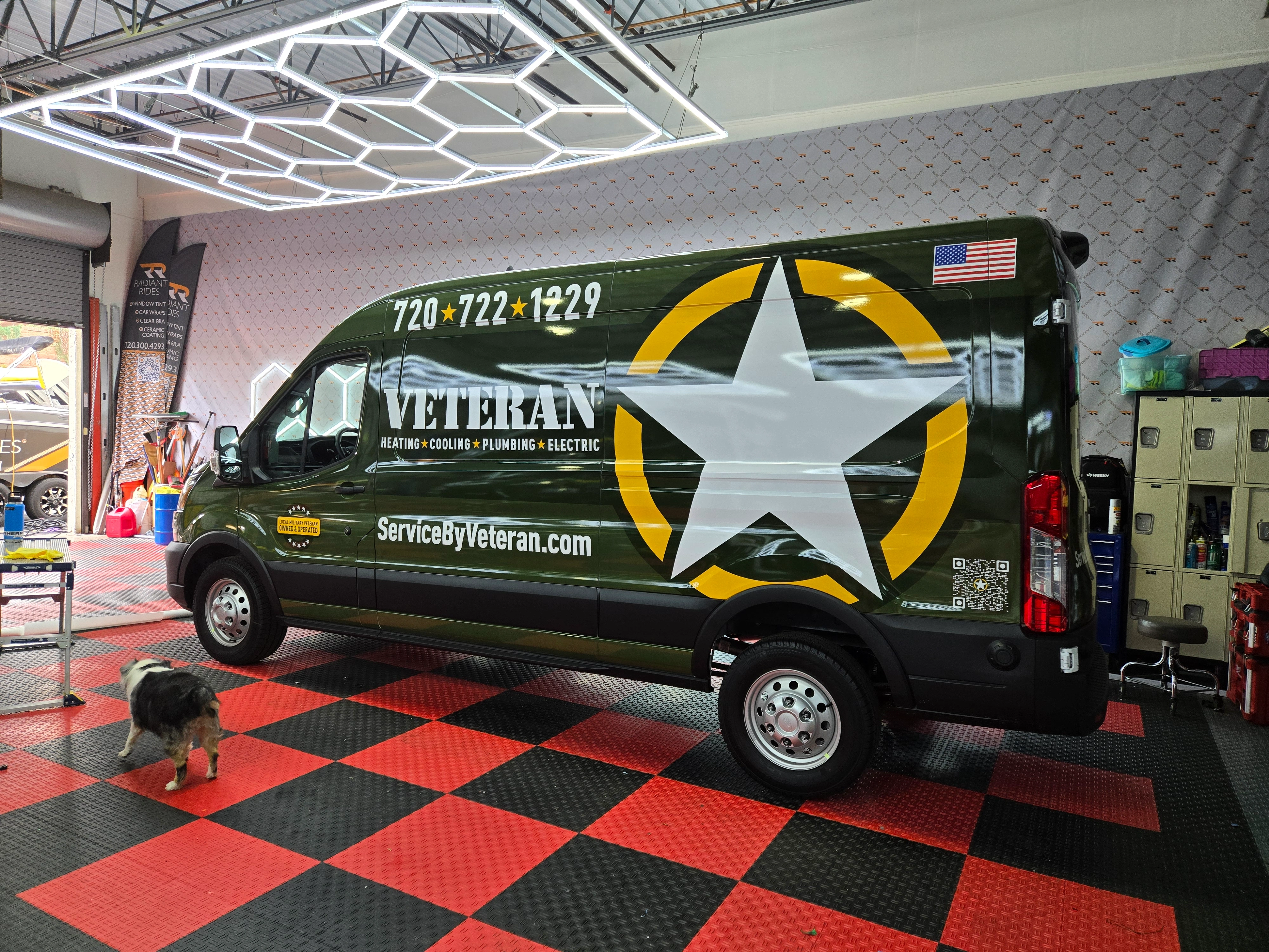 Green van in a garage with a large white star and yellow circle on the side. American flag decal, contact details, and a dog on red and black floor.