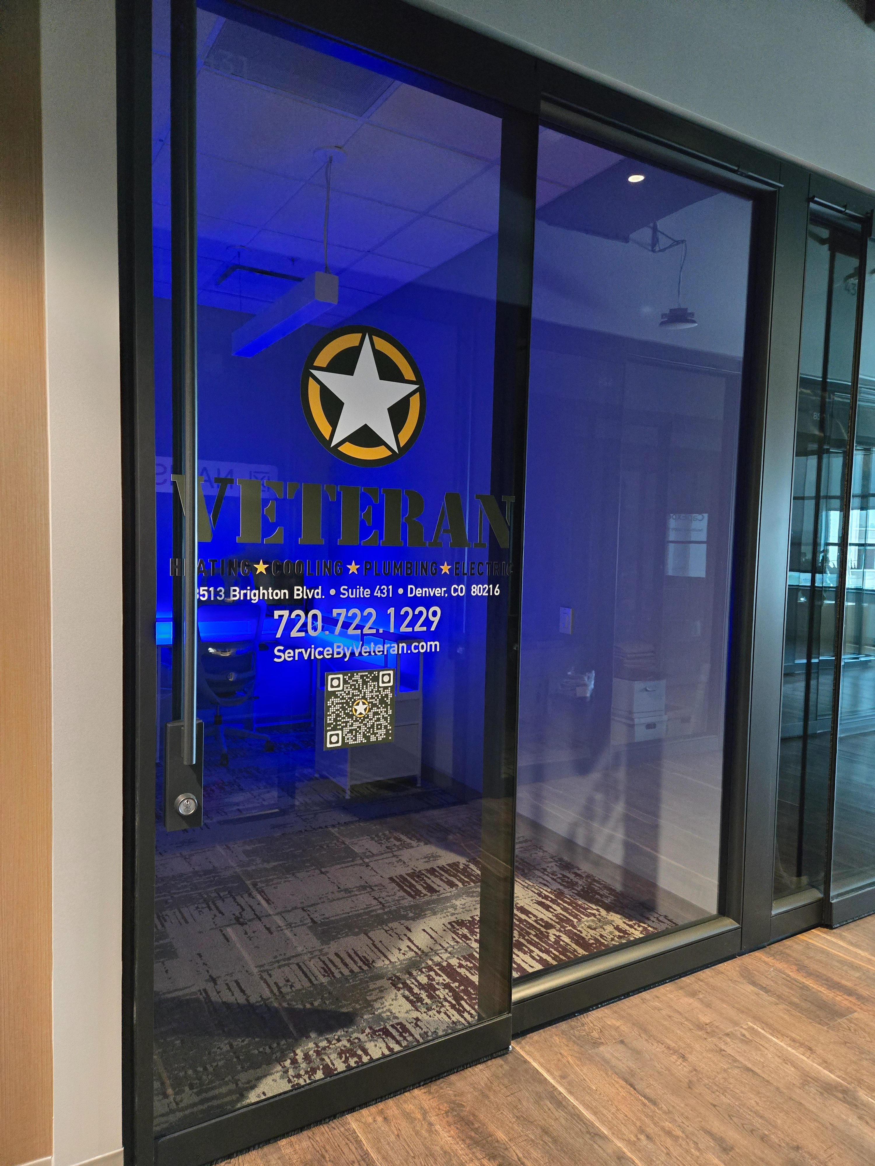 Glass office door with blue lighting, displaying a star logo and the word "Veteran." Contact info and a QR code are visible.