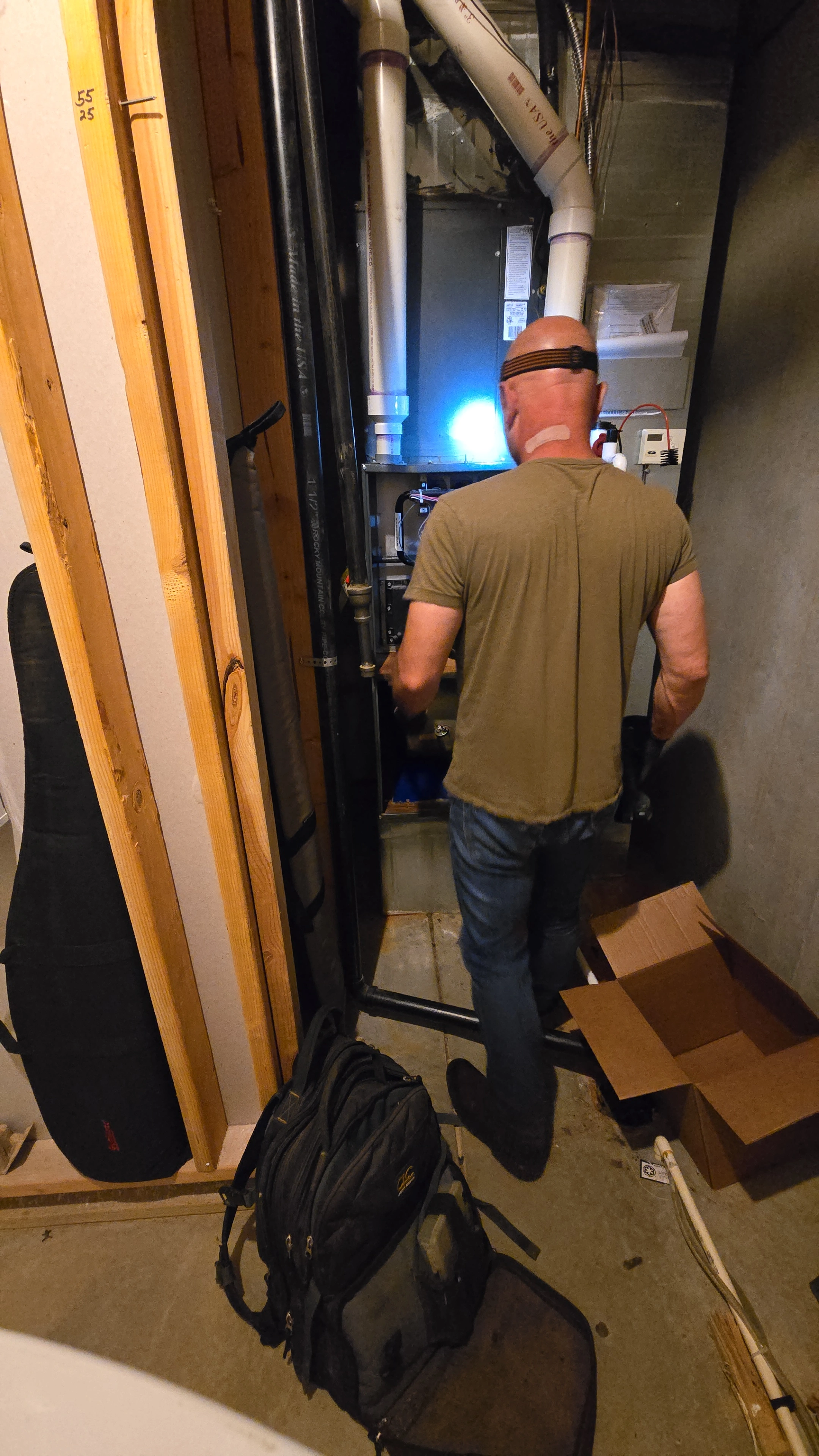 Un hombre con una lámpara frontal trabaja en una caldera en un cuarto de servicio poco iluminado.