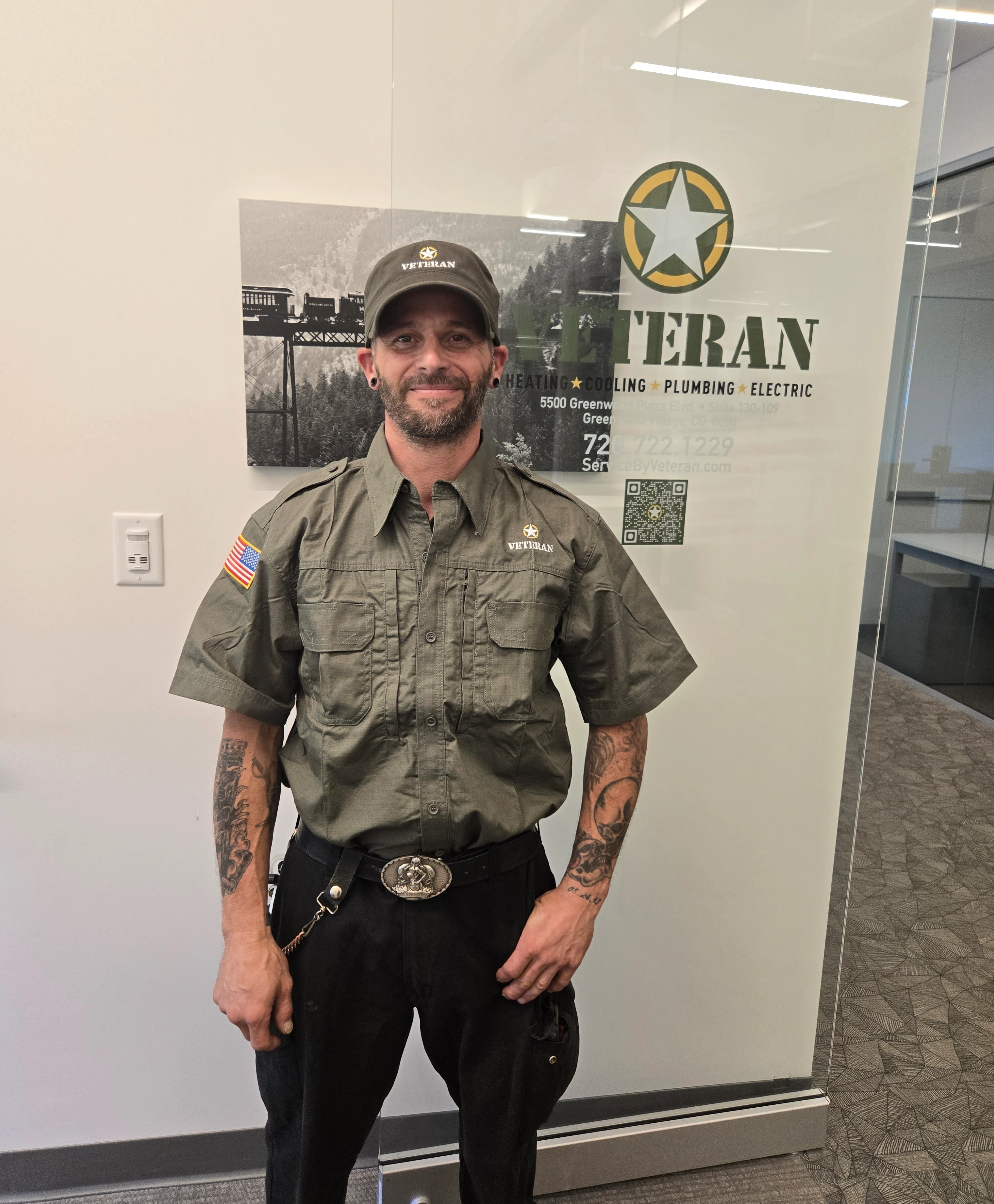 Un hombre con un uniforme y gorra de marca "Veteran" sonríe en una oficina.