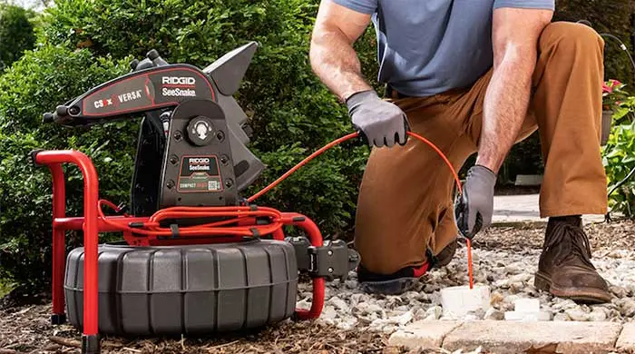 Worker feeding RIDGID camera into pipe.