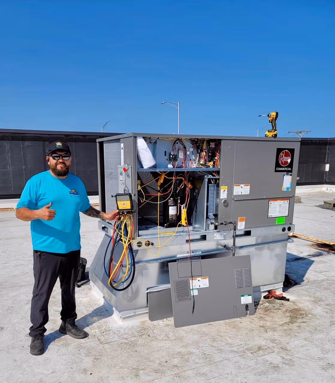 Man in a blue shirt gives a thumbs-up next to an open air conditioning unit on a rooftop.