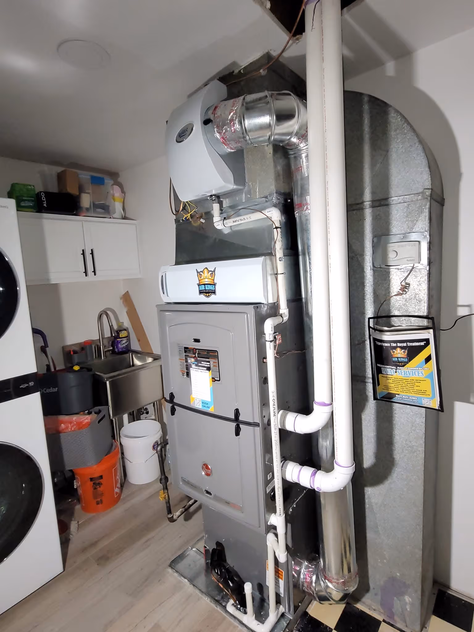 A washing machine and a large HVAC system with pipes are installed in a utility room.