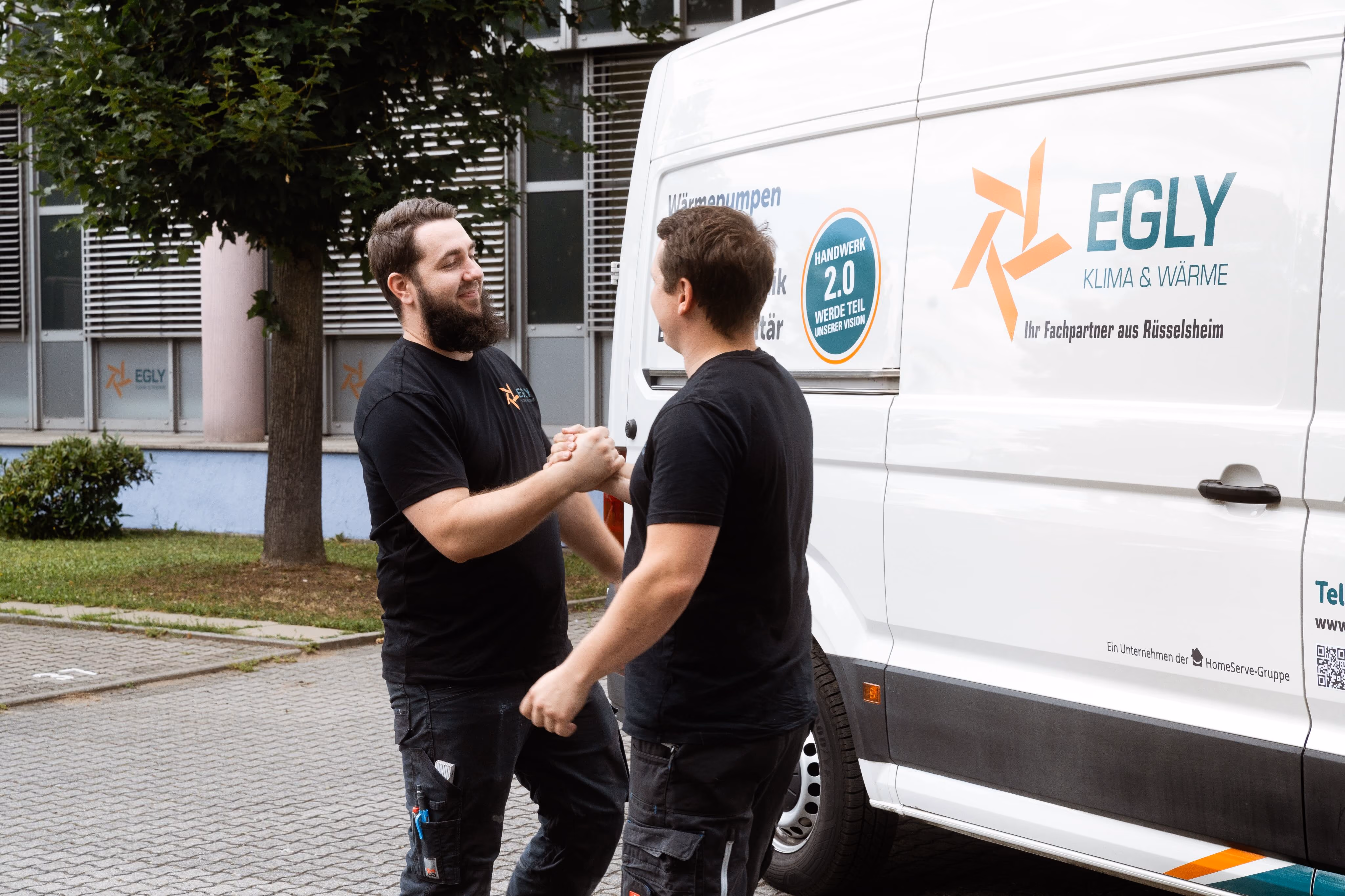 Zwei Mitarbeitende begrüßen sich am Servicefahrzeug.