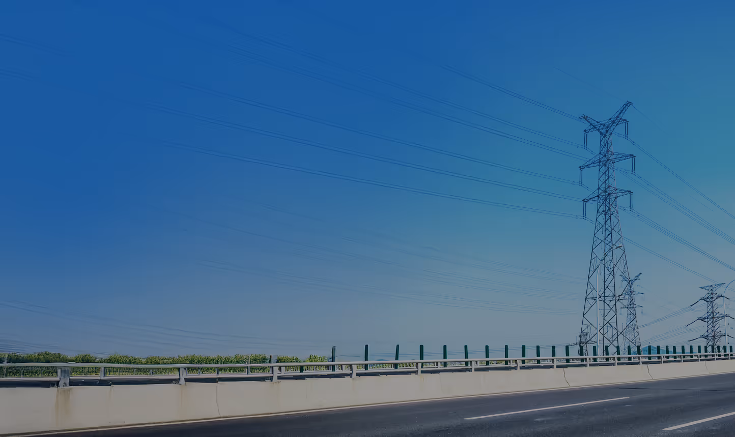 Empty highway road with guardrail and electrical transmission towers under a clear blue sky.