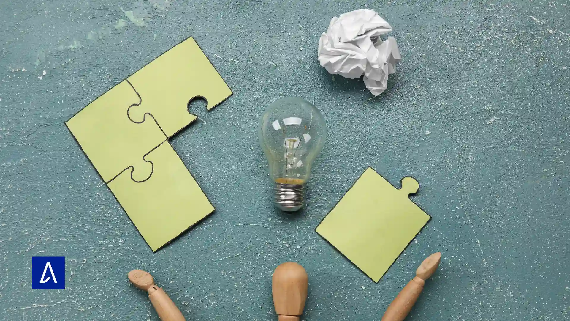 Ampoule posée au centre entourée de pièces de puzzle, d’un papier froissé et d’un mannequin en bois, symbolisant la créativité et les idées.