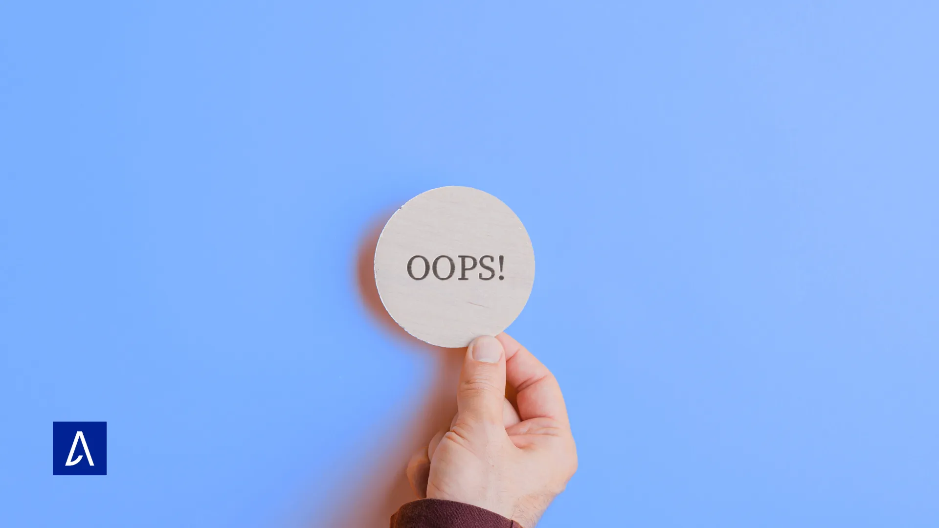 Main tenant un cercle en bois avec l’inscription « Oops! » sur fond bleu.