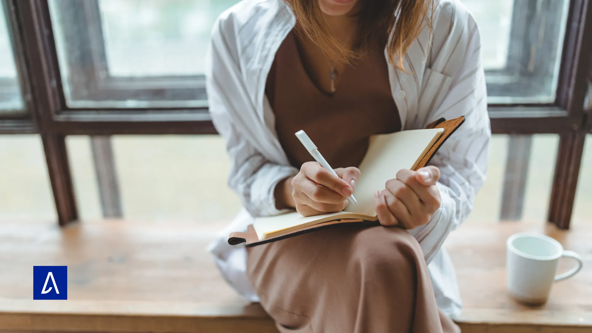 Femme assise près d’une fenêtre, écrivant dans un carnet, symbole de créativité et de copywriting.