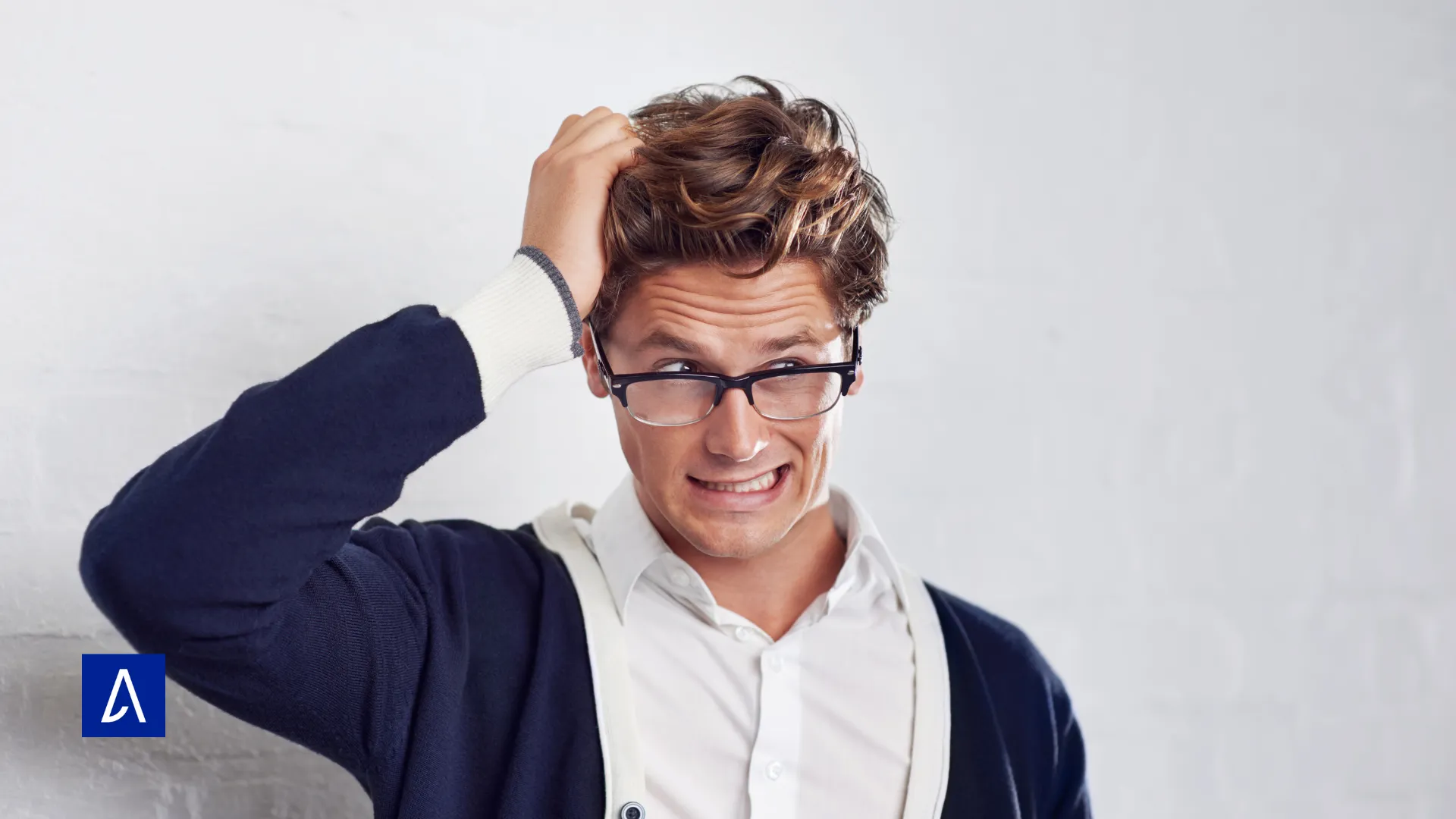 Homme avec lunettes et cardigan se grattant la tête avec une expression confuse.