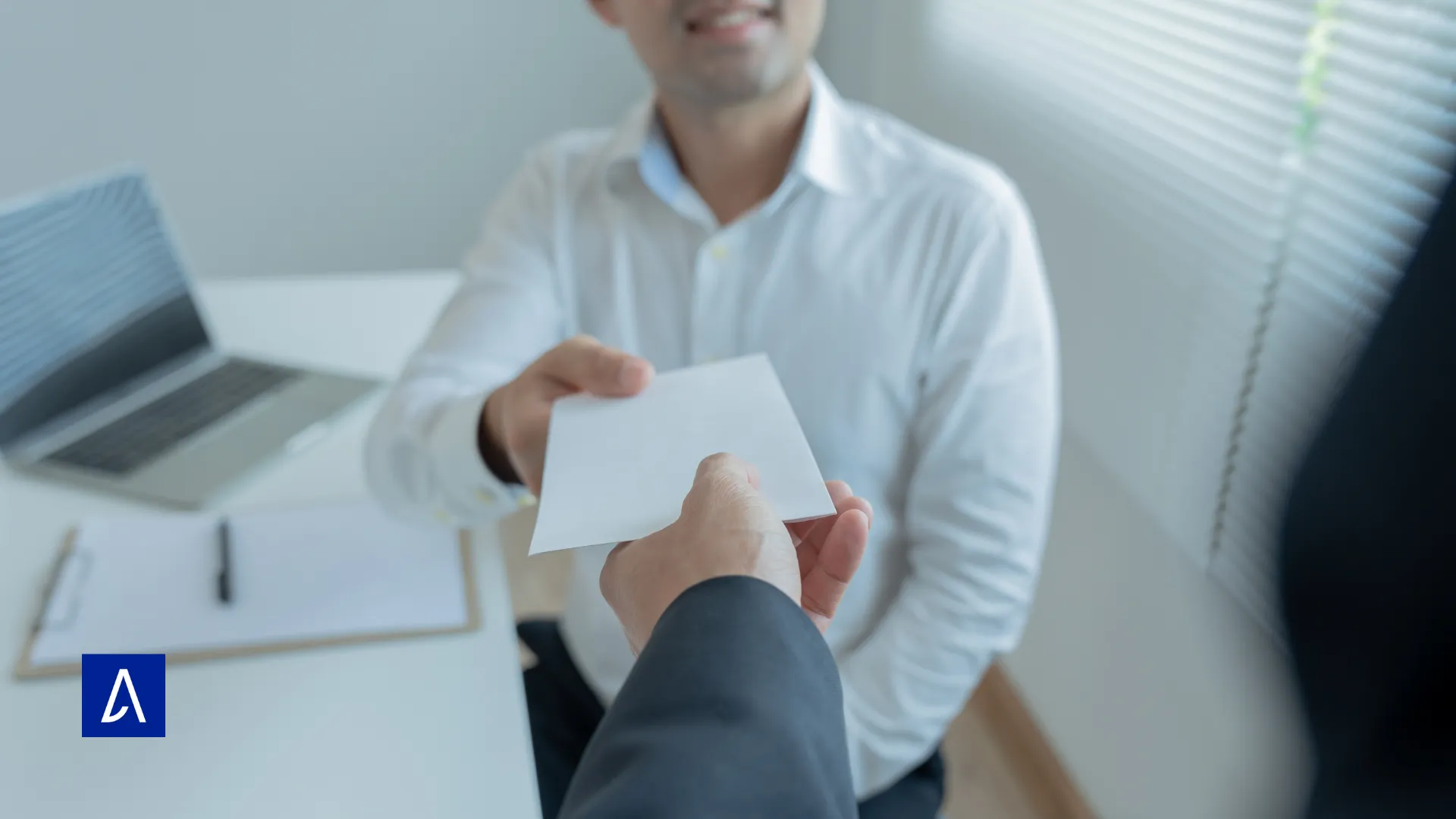 Homme tendant une enveloppe blanche à une autre personne dans un bureau.