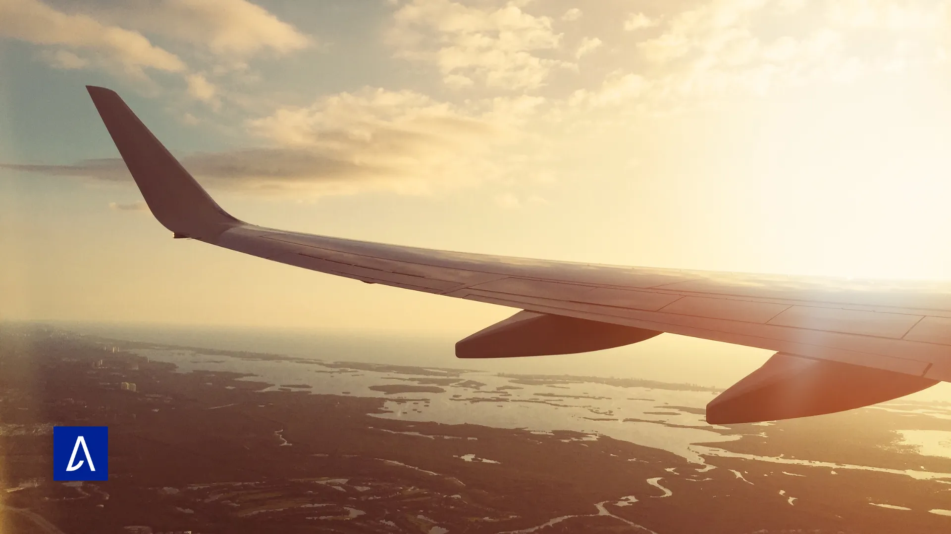 Vue d’une aile d’avion en vol au coucher du soleil, avec un paysage de lacs en contrebas.