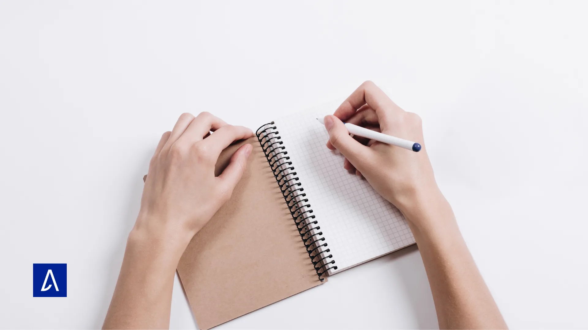 Personne écrivant dans un carnet à spirale sur une table blanche.