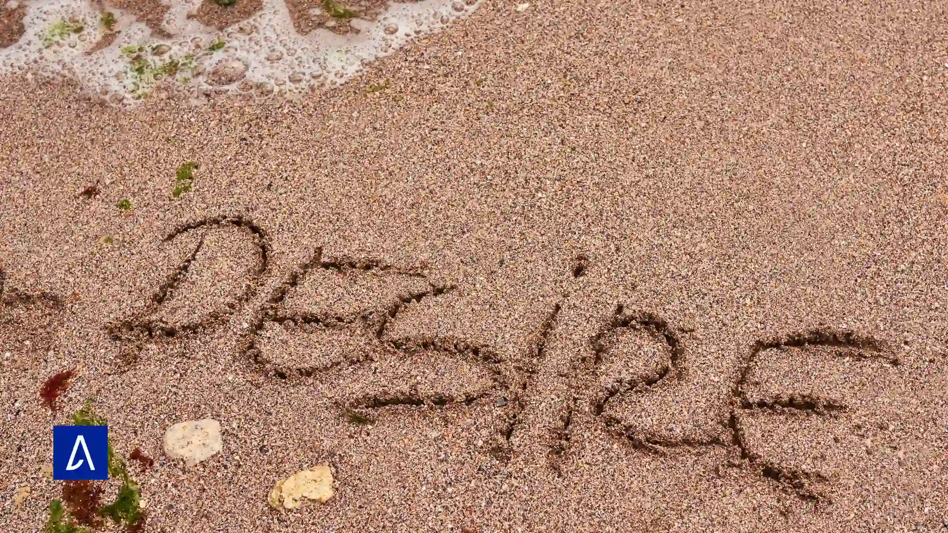 Mot “DESIRE” tracé dans le sable au bord de la mer, avec l’écume des vagues en arrière-plan.