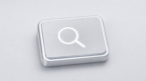Silberne Taste mit Suchlupe-Symbol auf hellgrauem Hintergrund.
