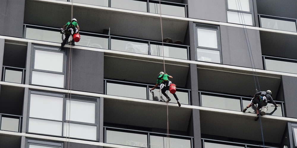 Three window washers suspended on ropes clean high-rise building exterior