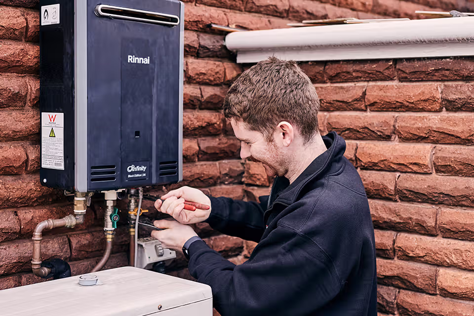 Technician repairing Rinnai water heater against brick wall